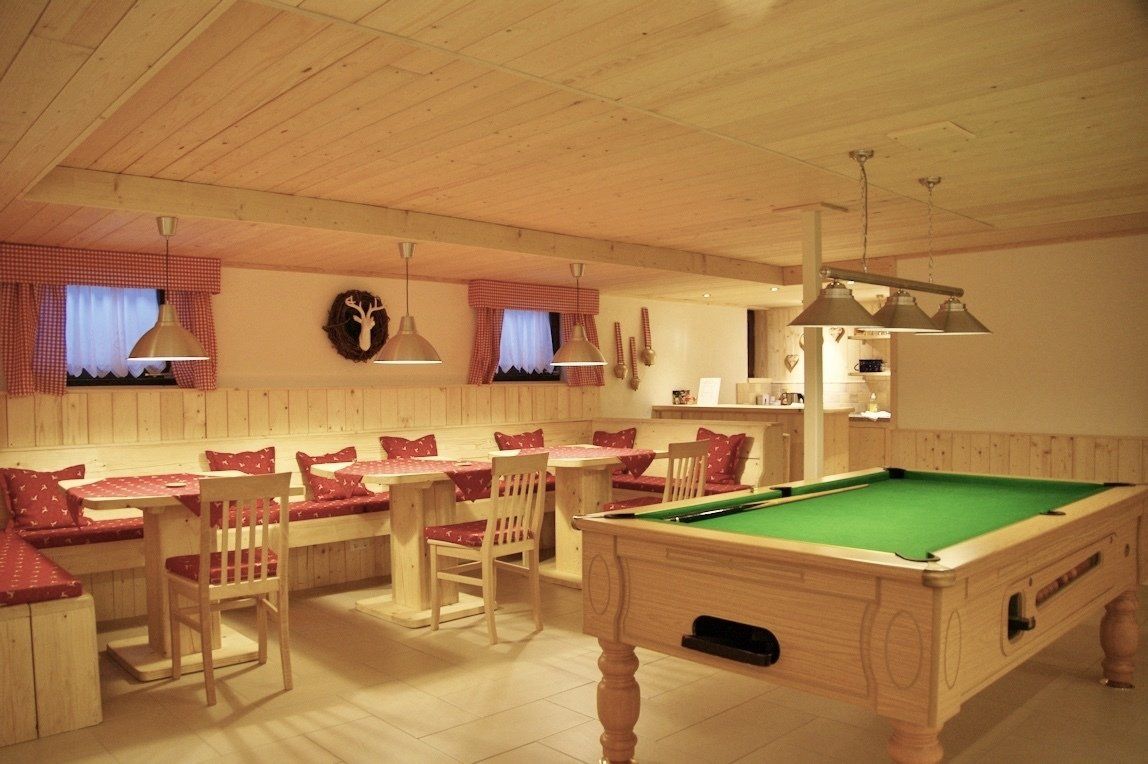 Spielzimmer mit Billardtisch und Essbereich, heller Holzvertäfelung und Pendelleuchten.