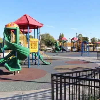 Tree Service Elmonte-Colorful playground with slides, climbing structures, and swings on a sunny day. Blue sky and trees in the background. Quiet, inviting atmosphere.