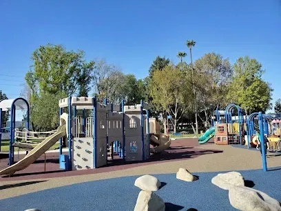 Tree Service Elmonte-Playground with slides, climbing structures, and soft surfaces under a clear blue sky. Trees in the background create a vibrant, inviting atmosphere.