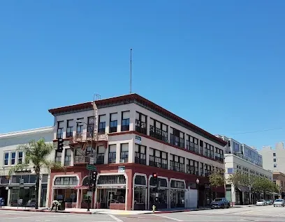 Tree Service El Monte Ca - Three-story historic building on a sunny street corner, featuring arched windows and a fire escape. Palm trees and blue sky create a serene urban scene.