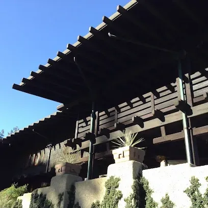 Tree Service Elmonte-Large wooden structure with overhanging roof and support beams, surrounded by planters on a sunny day. Minimalist and serene architectural design.