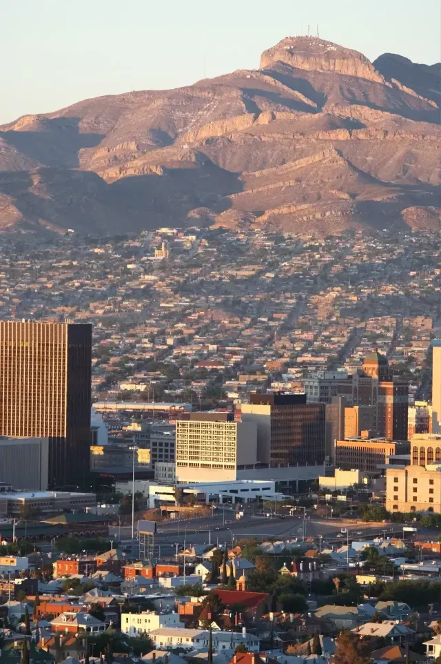 Tree Service El Monte Ca - Aerial view of a city with colorful homes and modern buildings, framed by rugged mountains under a clear sky during sunset.