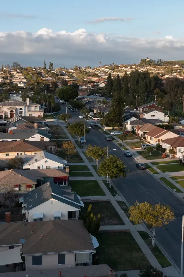 Tree Service El Monte Ca - Aerial view of a suburban neighborhood featuring houses, tree-lined streets, and distant hills under a partly cloudy sky.