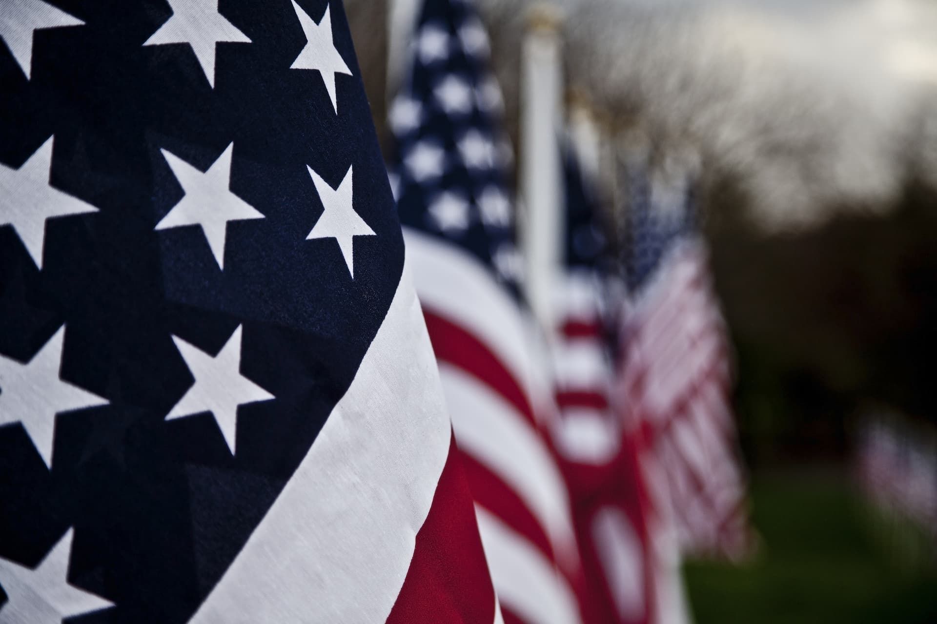 American flags in a row, with one large flag in the foreground and others blurred behind it outdoors
