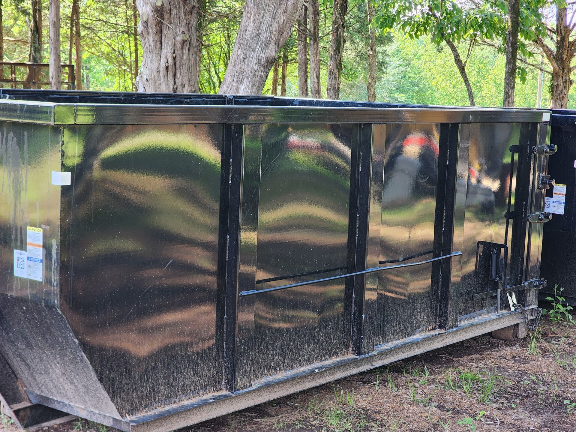 A large metal dumpster is sitting in the middle of a forest.