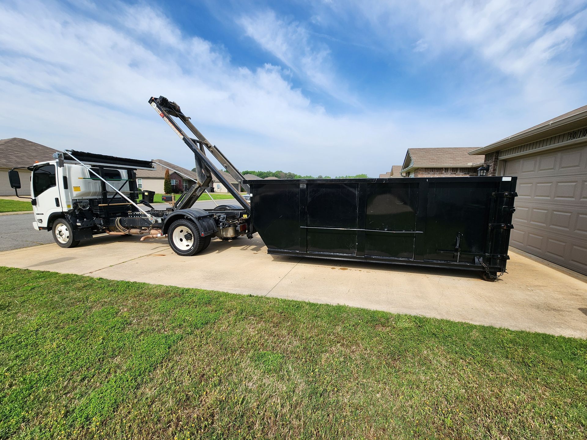 A dumpster truck is loading a dumpster in a driveway.