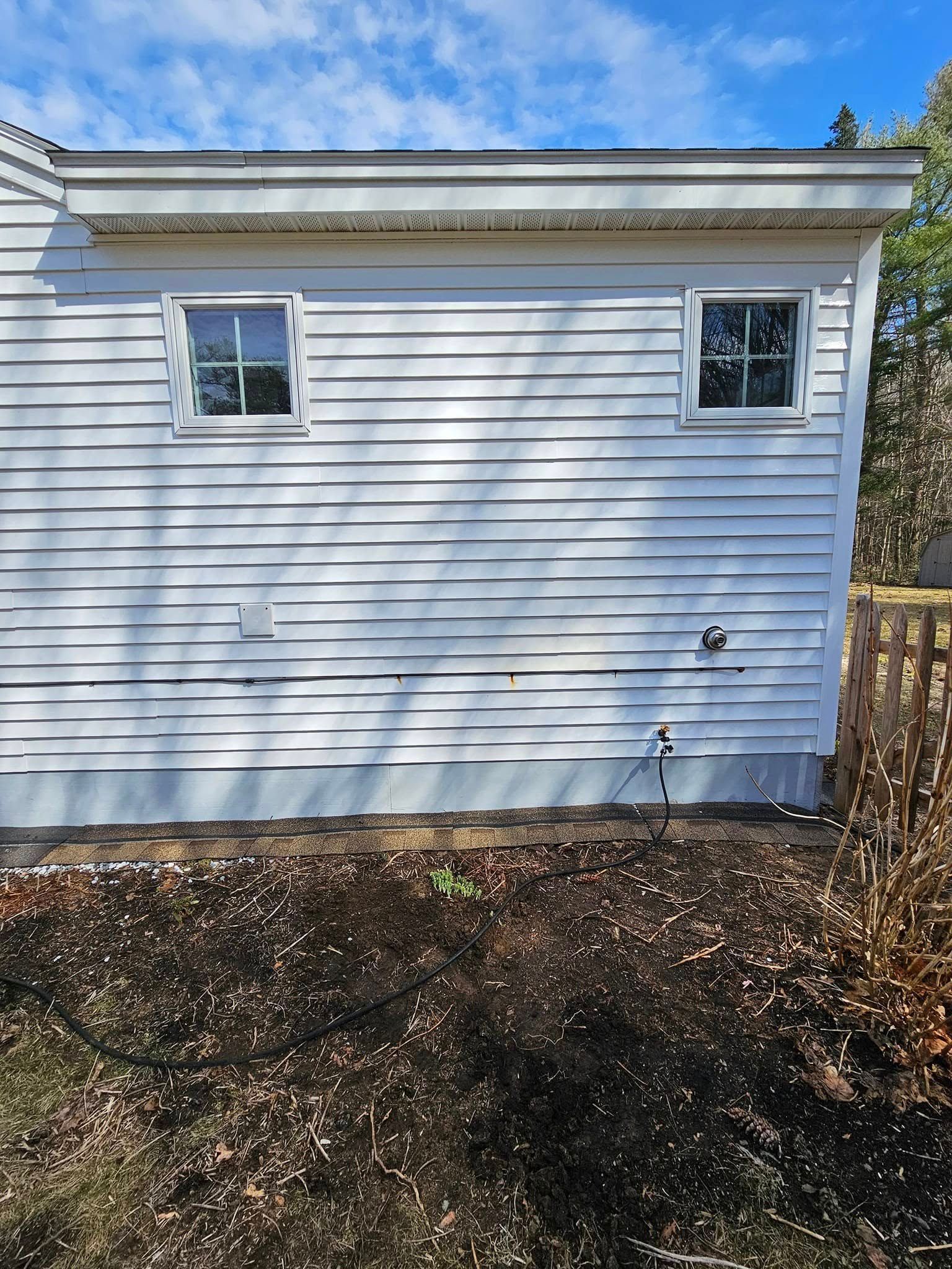 A worker in a lift basket uses a pressure washer to clean a shingled roof on a brick house.