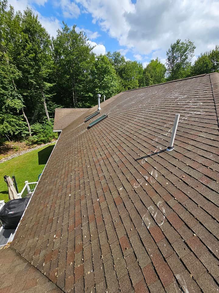 A person wearing safety gear pressure washes a tiled roof.