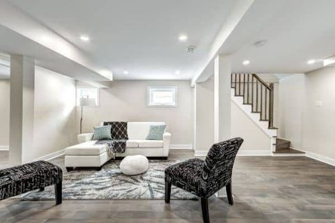 Bright modern living room with white sofa, black chairs, gray rug, and staircase to the right.