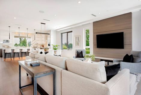 Bright modern open-plan living room with beige sofa, wall-mounted TV, and kitchen in the background