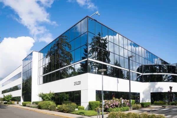 Modern glass office building with reflective windows and white facade under a blue sky