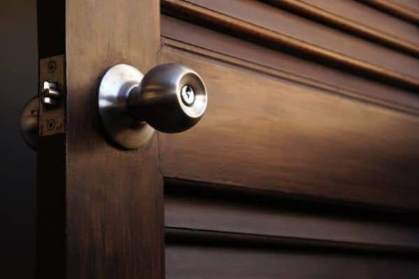 Silver door knob on a dark wooden louvered door