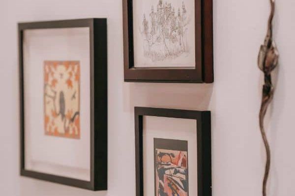 Three framed art prints on a white wall beside a hanging decorative branch