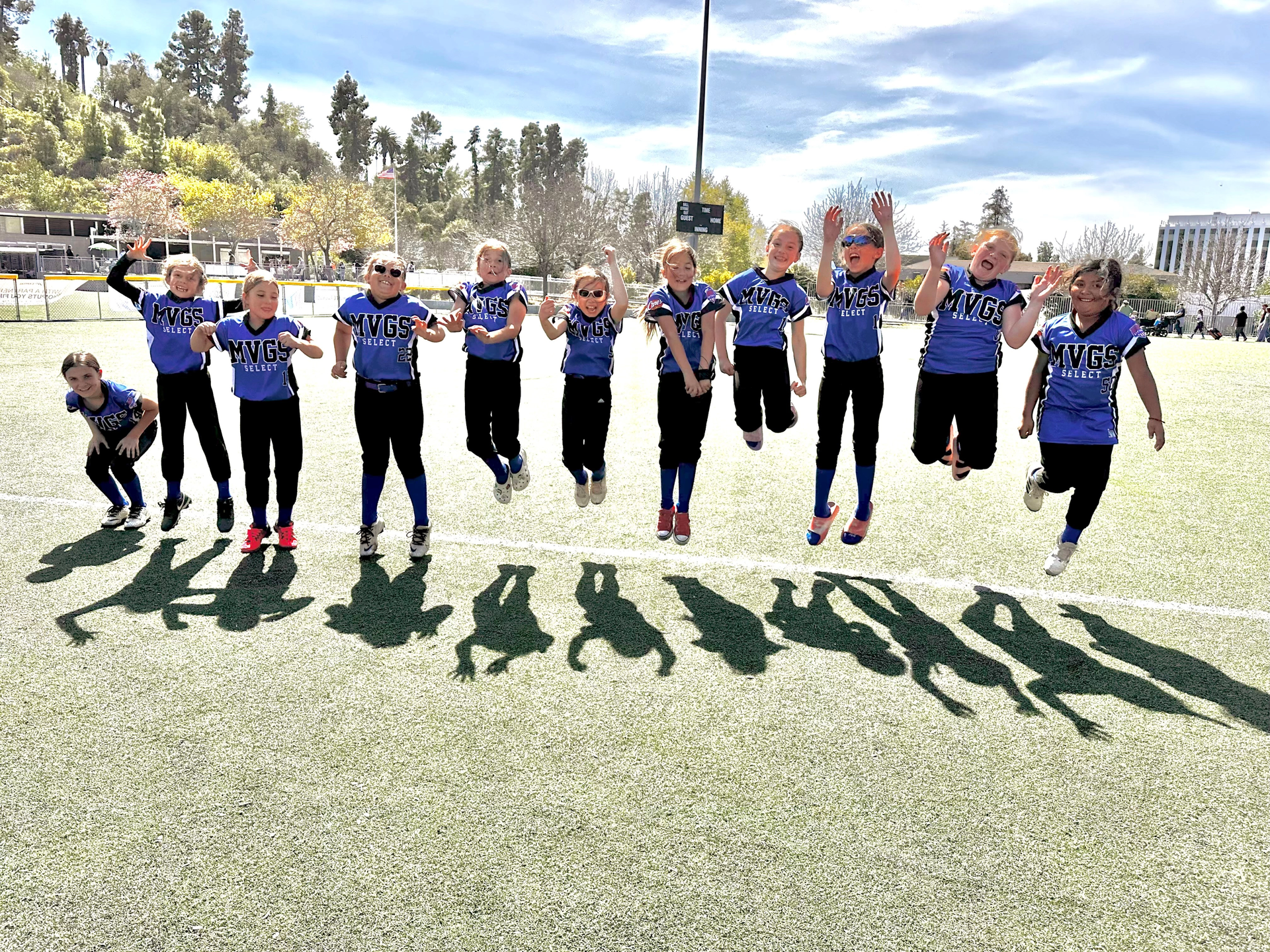 Softball team in blue uniforms, celebrating a win with high-fives and hugs on the field.