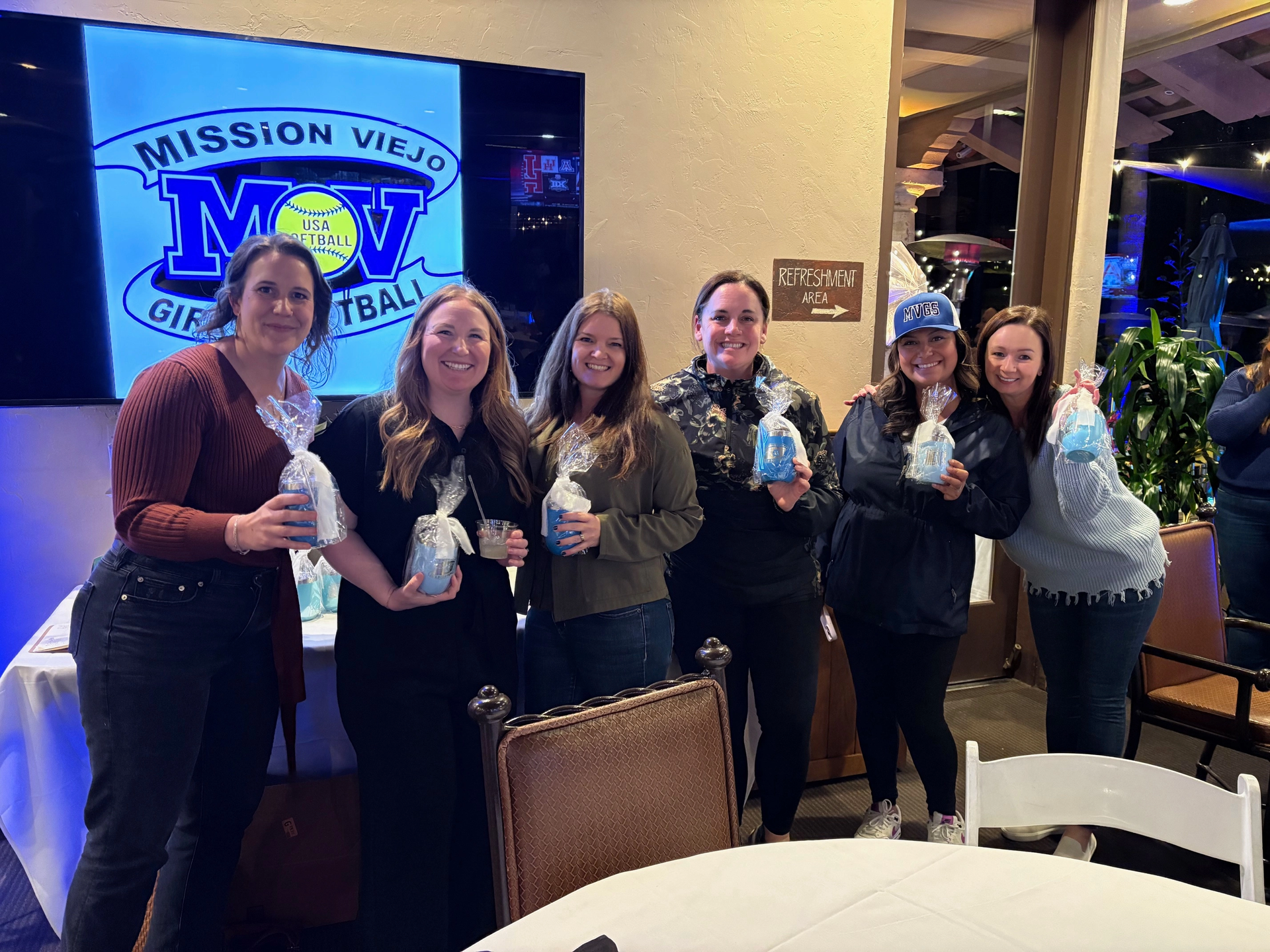 Six people smiling, holding gifts, posing at a Mission Viejo Girls Softball event.