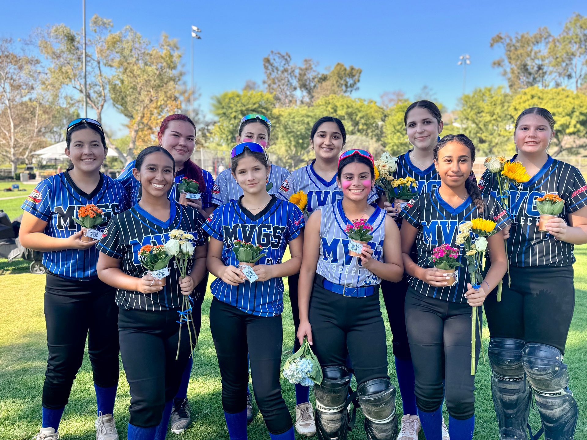 Softball team in blue jerseys, holding flowers, on a sunny field.