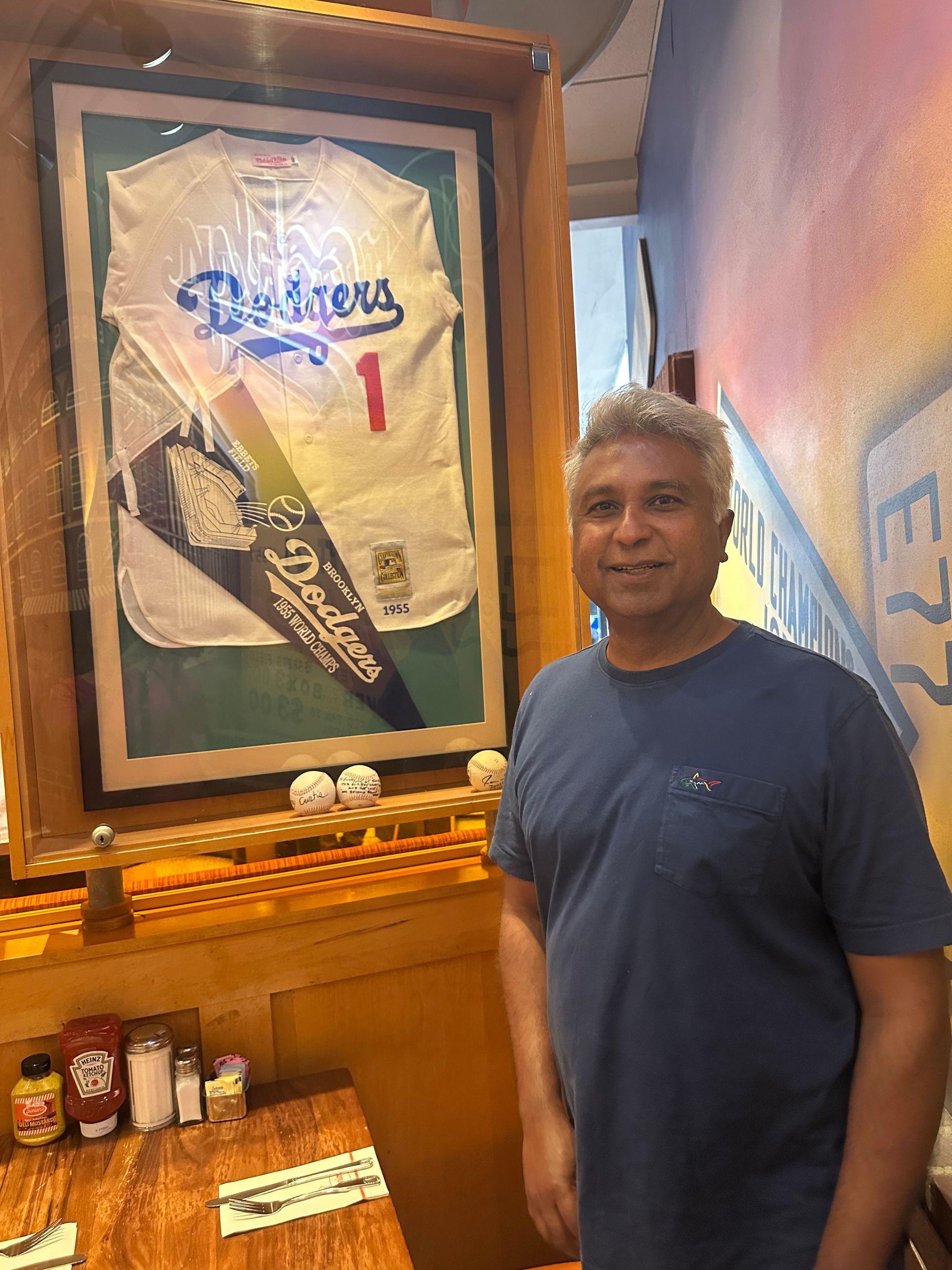 Man standing next to a framed baseball jersey and pennant, restaurant setting.