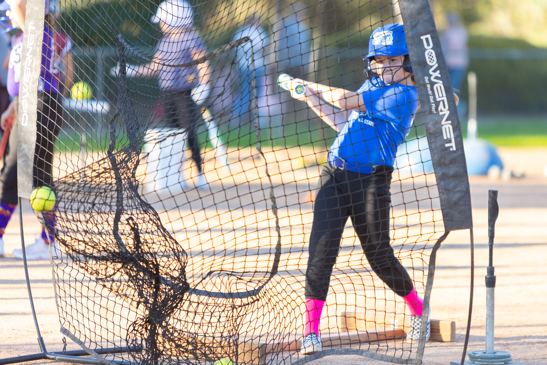 Softball player in blue shirt batting, practicing swing into a net.