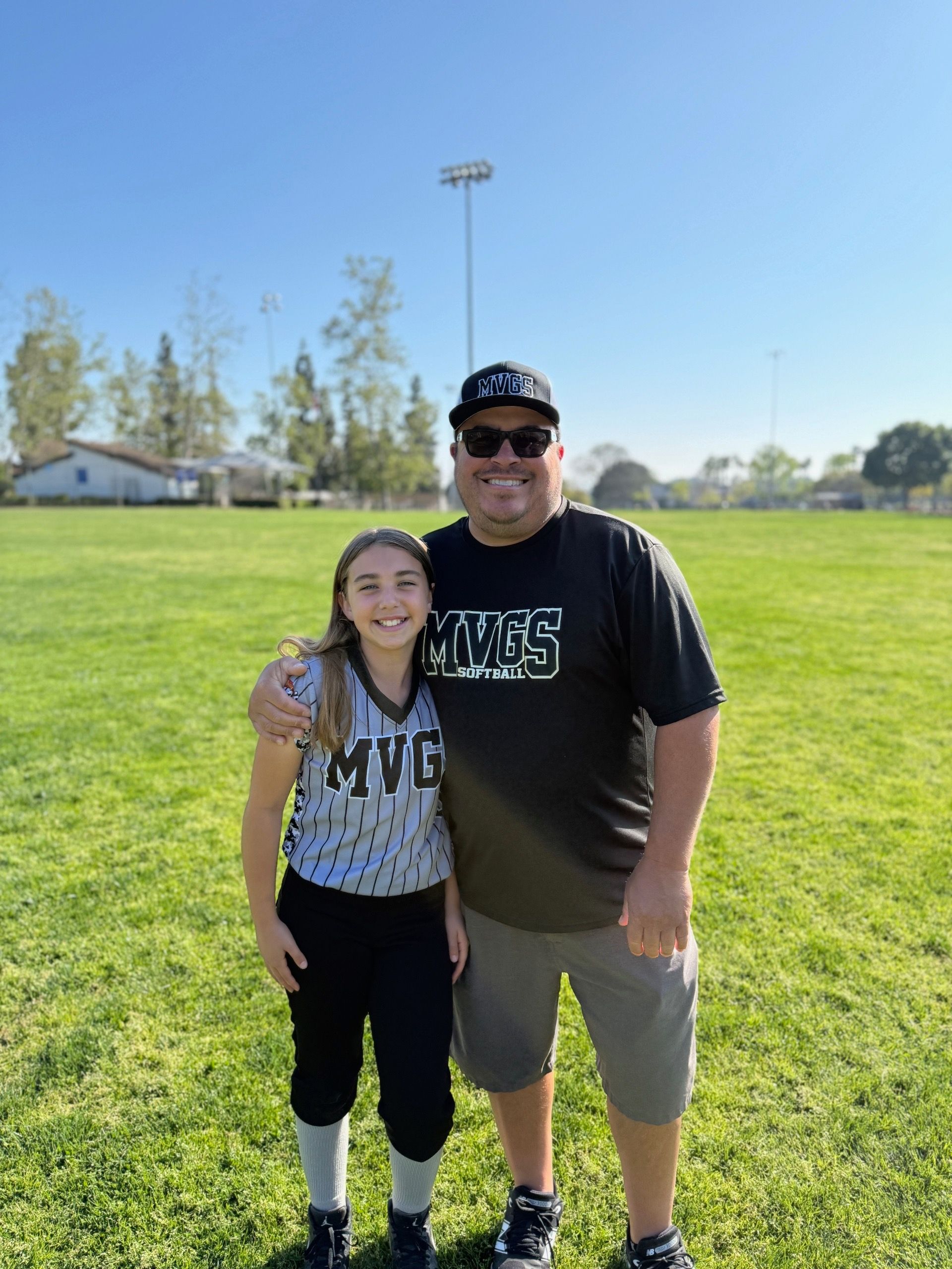 Person wearing a sash and hat with a balloon, smiling, standing in front of a chain fence with a blue cart.