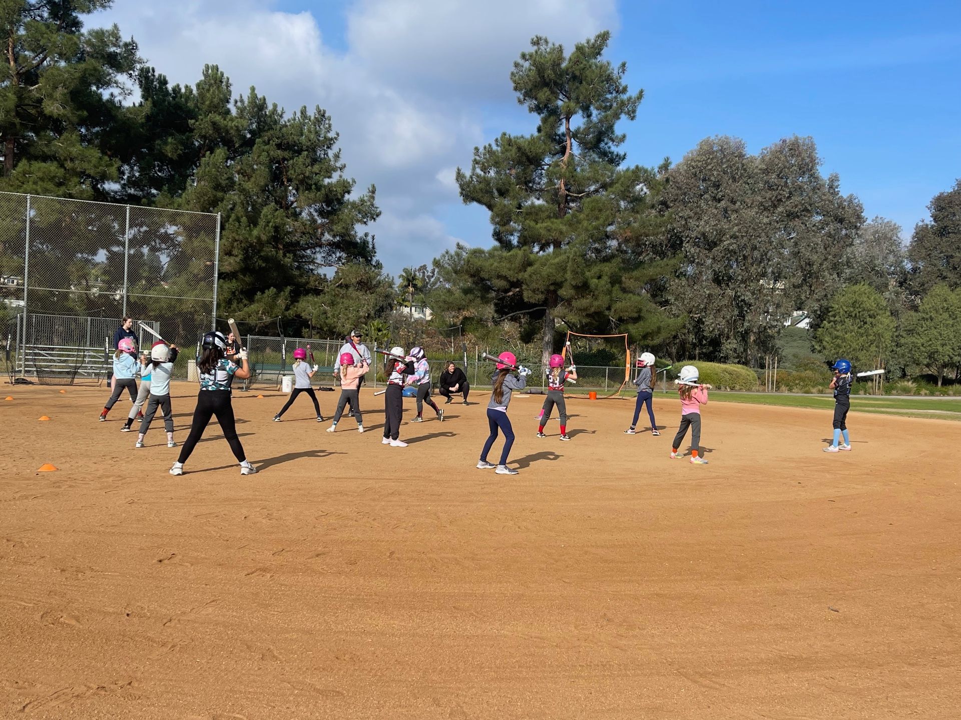 Children playing softball on a brown field under a sunny sky; trees in the background.