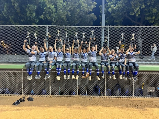 Youth softball team holding a banner, celebrating a tournament win, wearing team uniforms.
