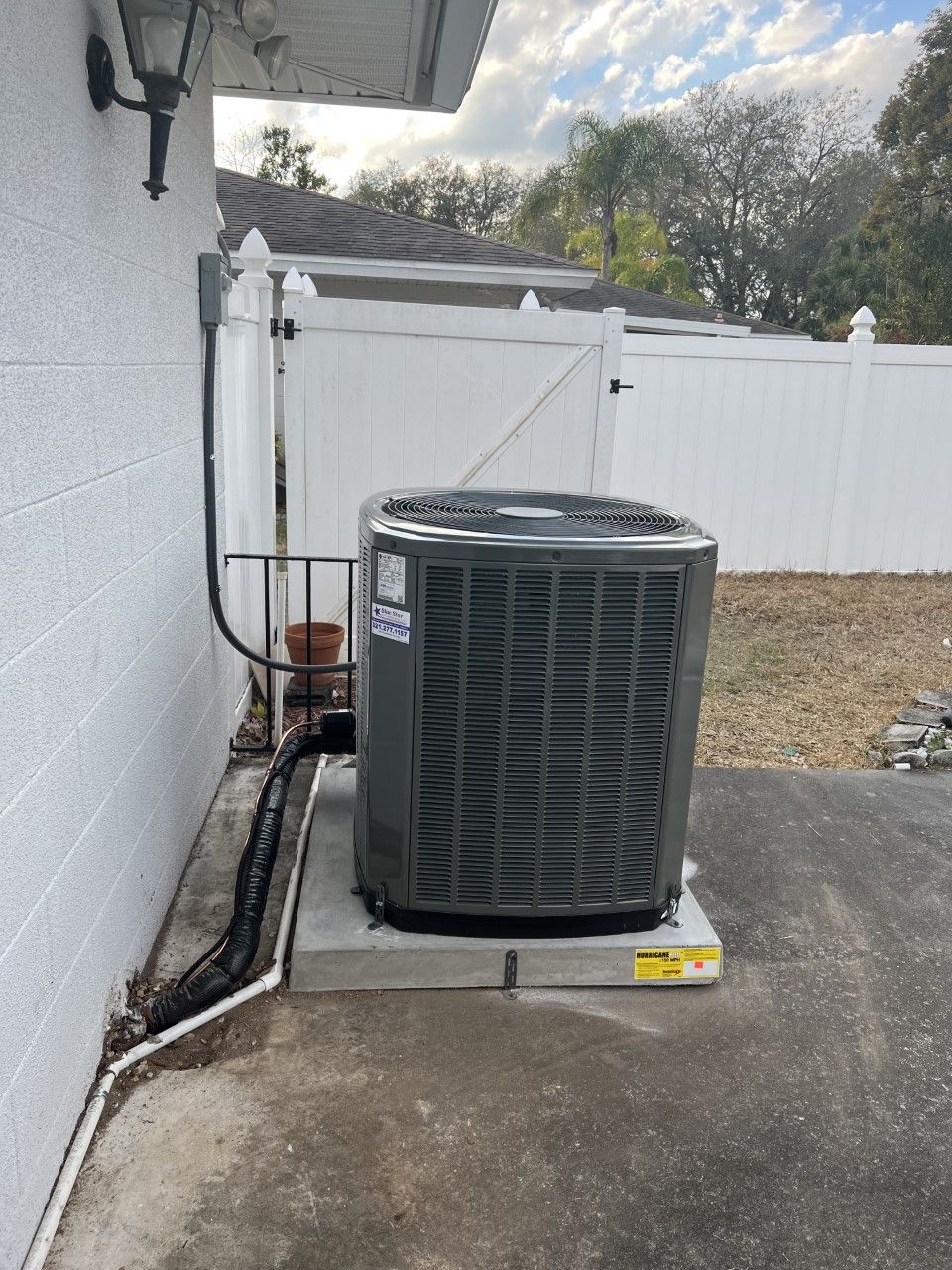 an Astoria Heating & Cooling
air conditioner is sitting on the side of a house next to a white fence.