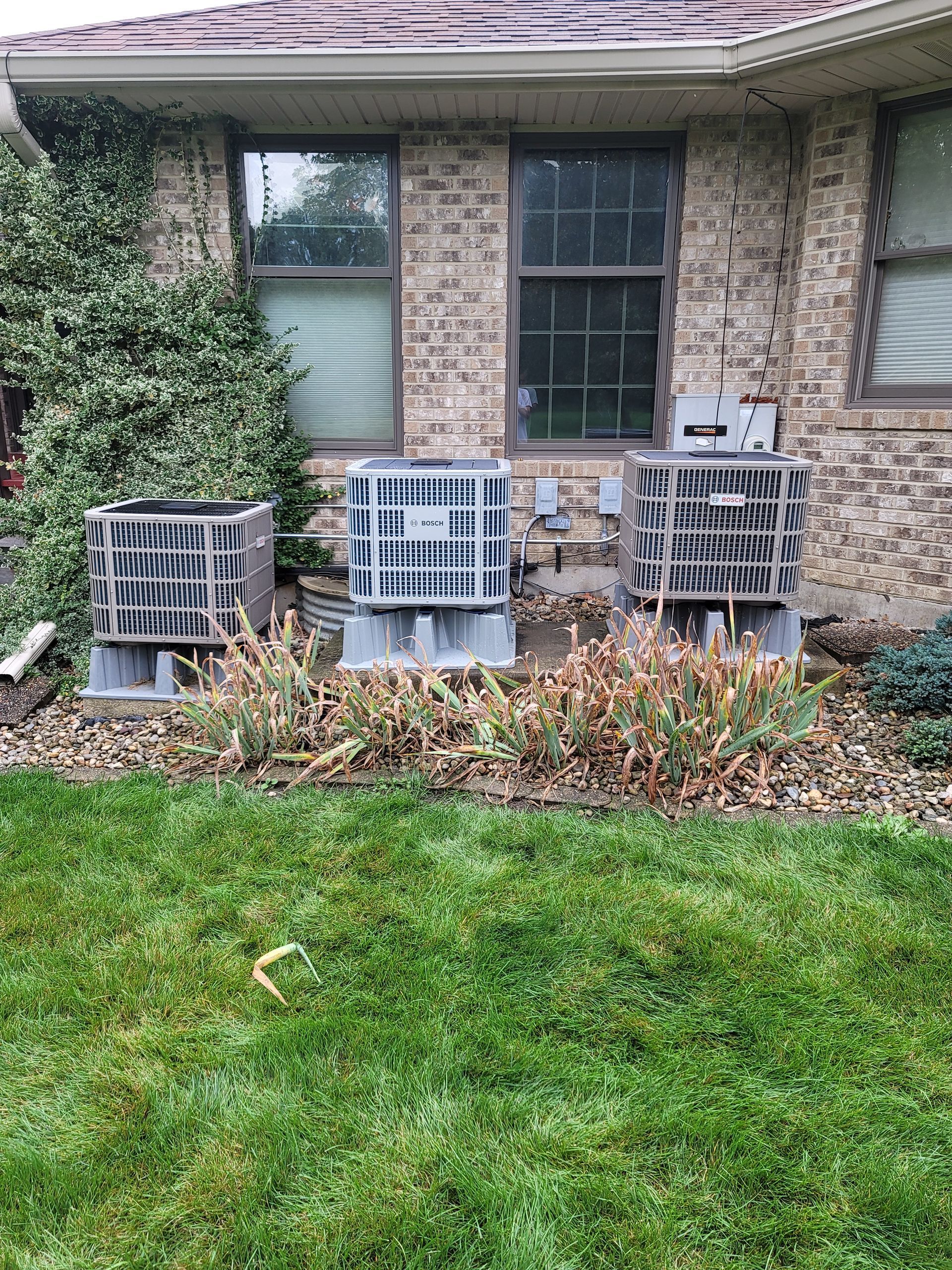 three air conditioners are sitting in front of a brick house .