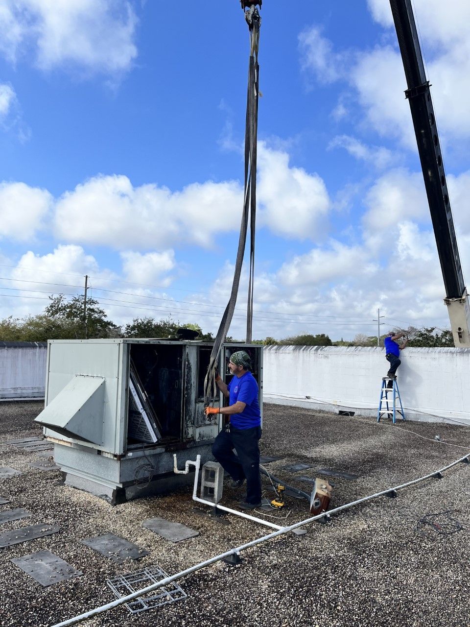 An Astoria Heating & Cooling technician is working on an air conditioner on a roof with a crane.