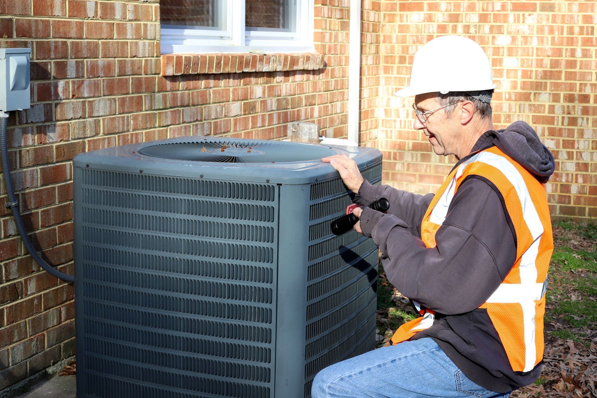 An HVAC technician inspecting an outdoor AC unit during a winter tune-up in Longwood.