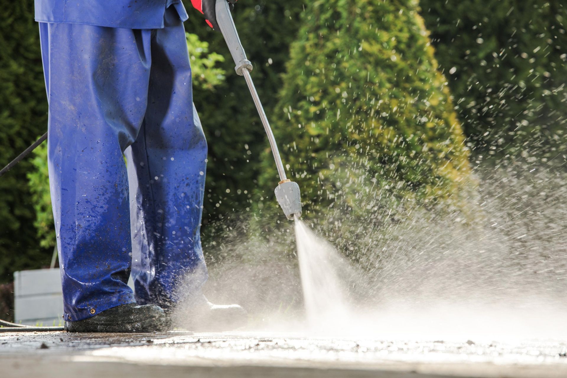 Person in blue overalls power washing a concrete surface.