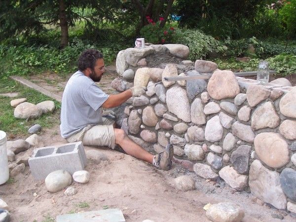 A man is sitting on the ground working on a stone wall