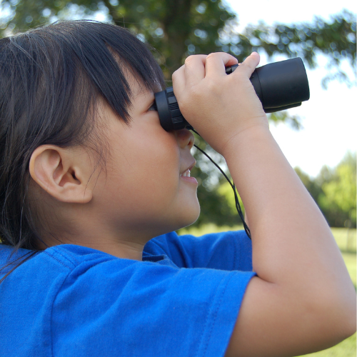 A little girl in a blue shirt is looking through binoculars