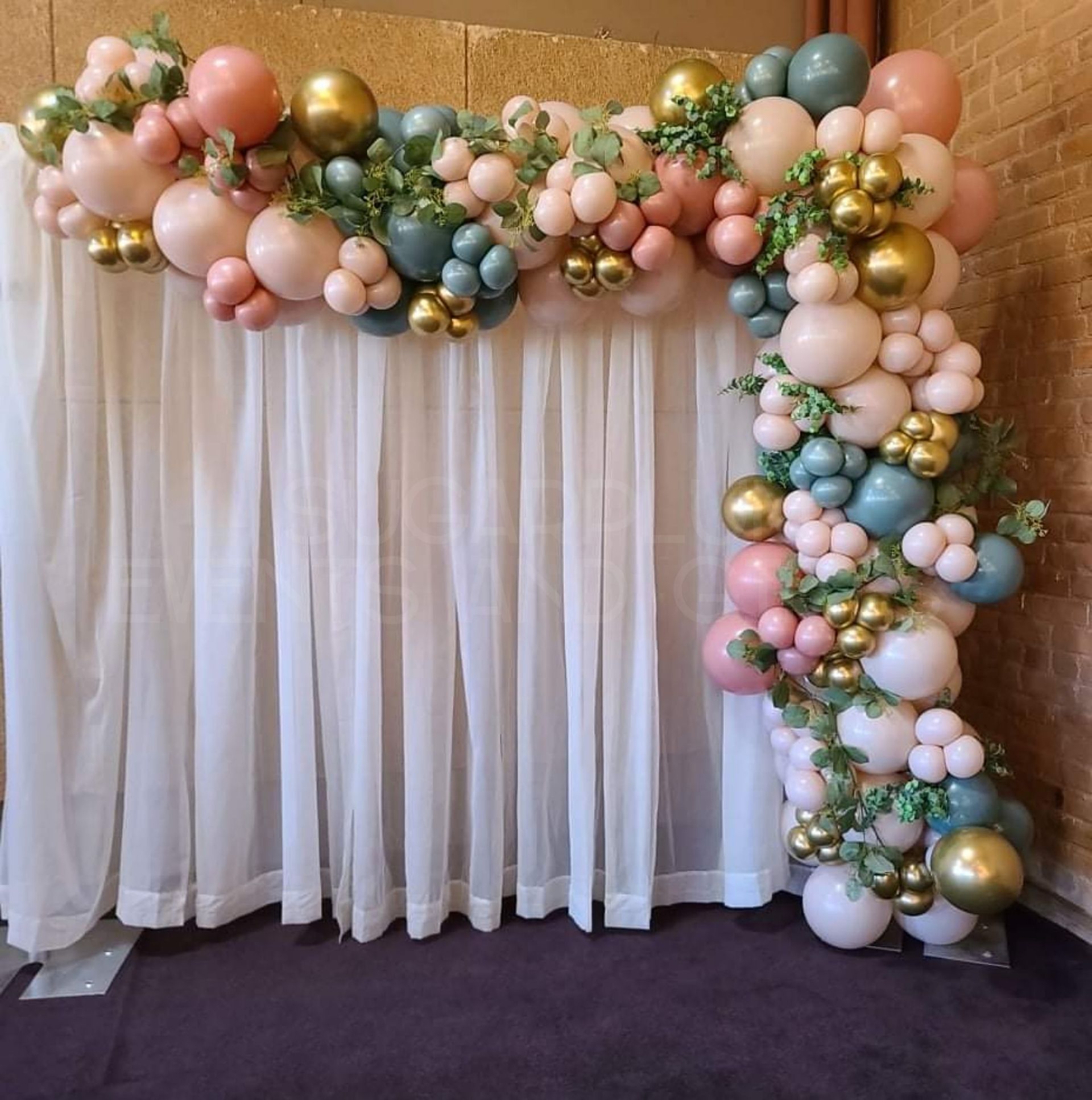 Pastel pink, blue, and gold balloon garland framing a white draped backdrop
