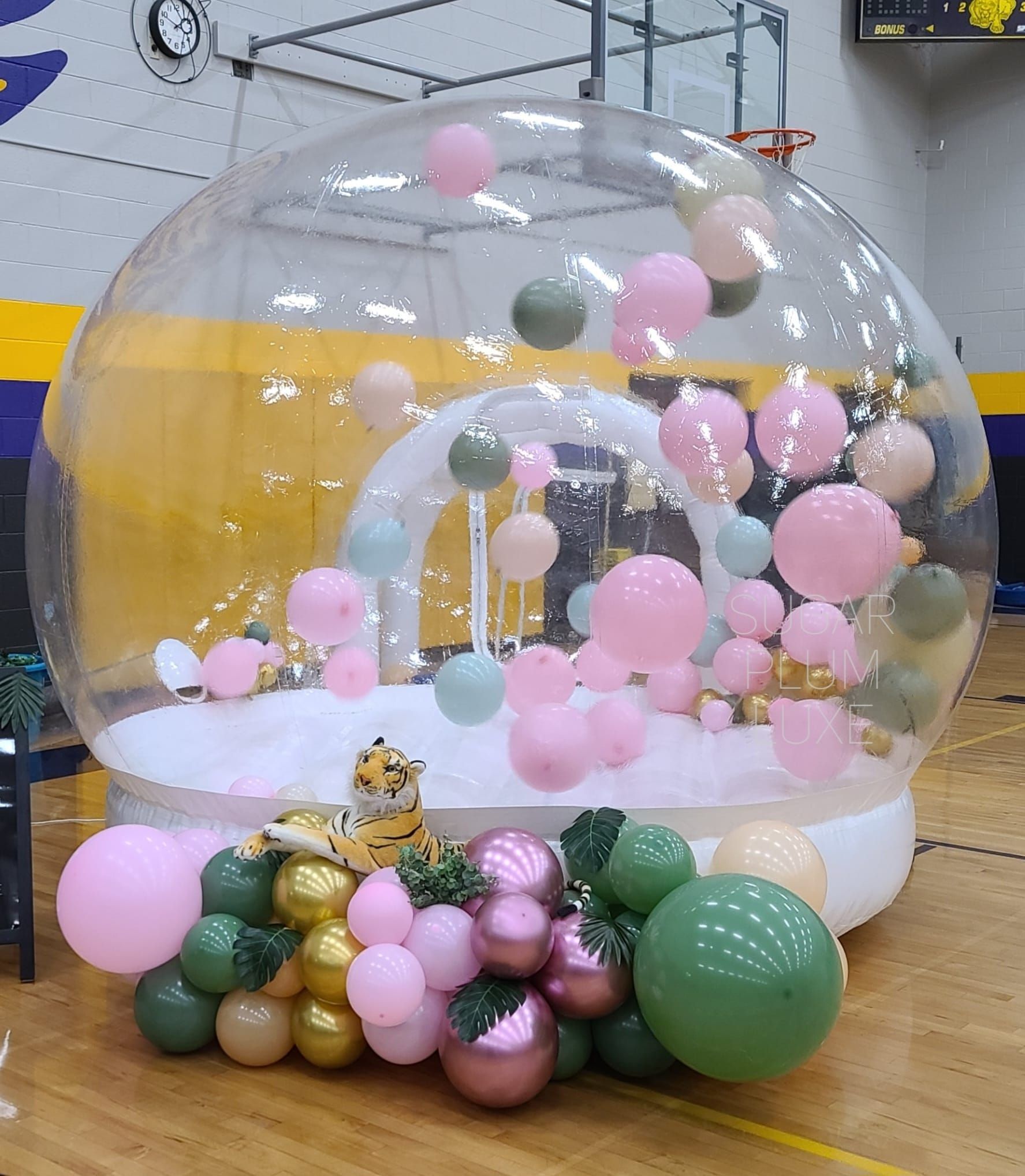 Clear balloon dome filled with pink and gold balloons, set on a white base in an indoor play area