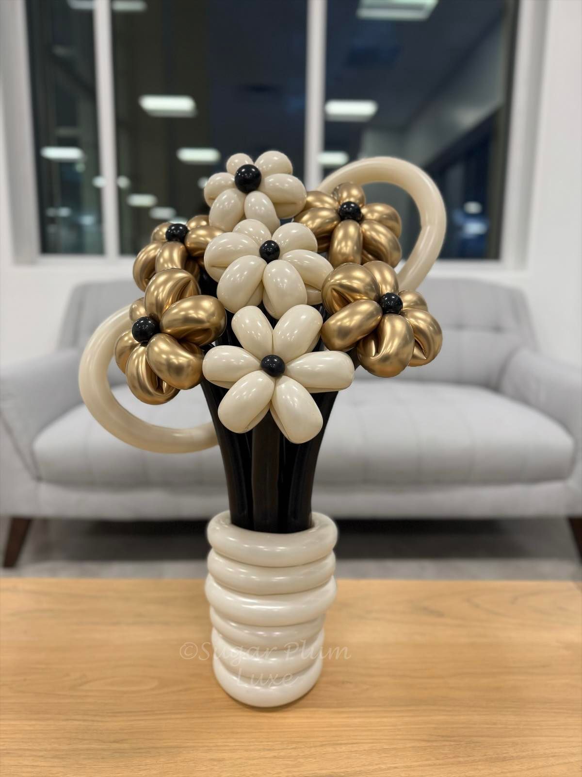 Balloon flower bouquet in a white vase on a wooden table, with a couch in the background