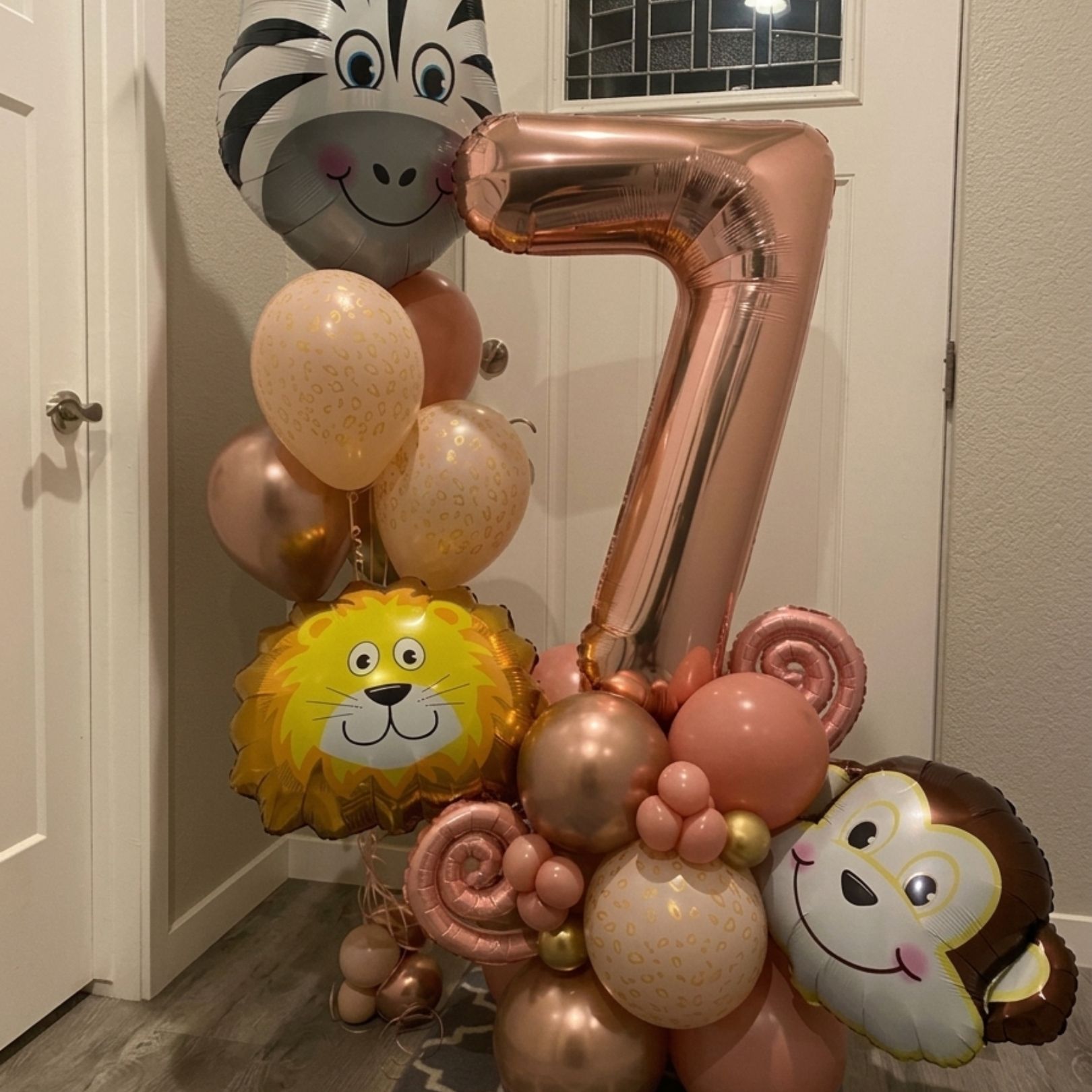 Balloon birthday display with a rose-gold number 7 and cartoon animal balloons in a hallway