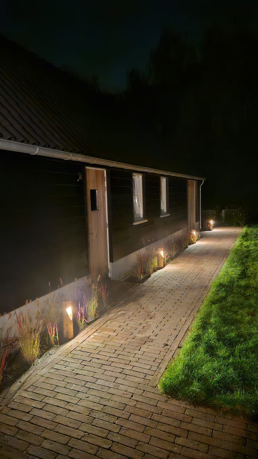 Een pad verlicht met warme lampen langs een donker gebouw met ramen 's nachts.