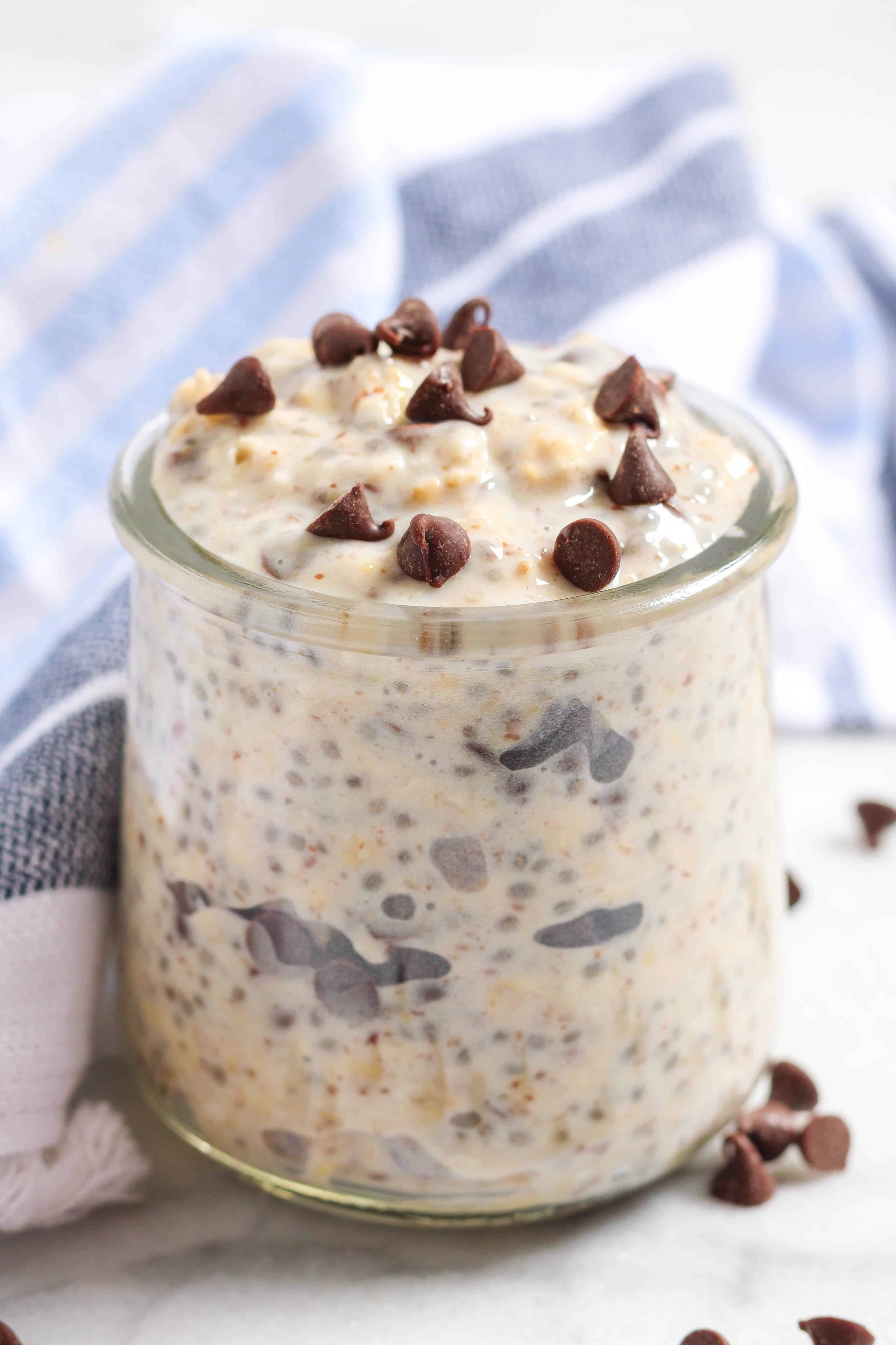 Overnight oats in a glass jar topped with chocolate chips on a white surface with a blue-striped towel.