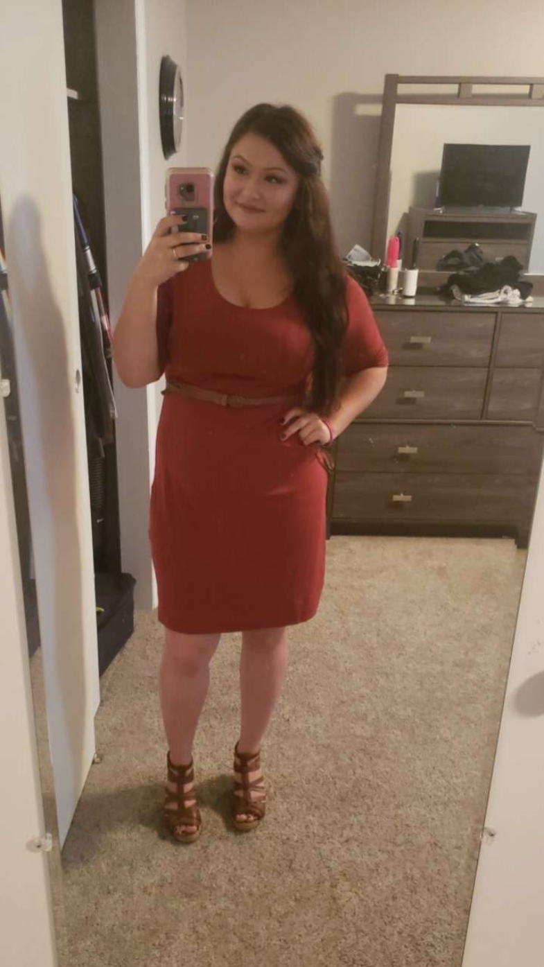 Woman in red dress and heels takes selfie in bedroom.