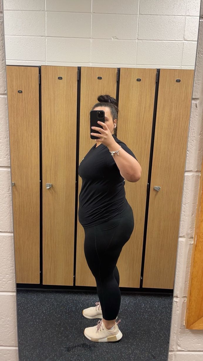 Woman in black workout clothes and sneakers poses in gym mirror.