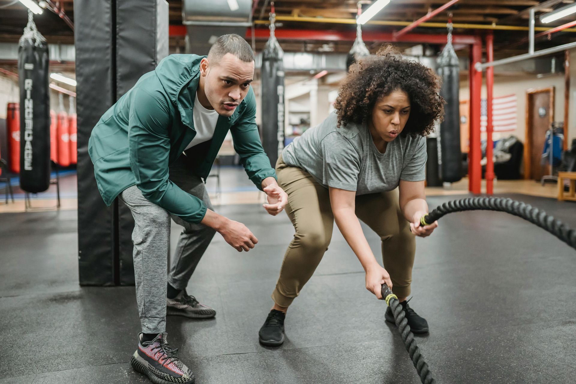 Man instructing woman using battle ropes in a gym.