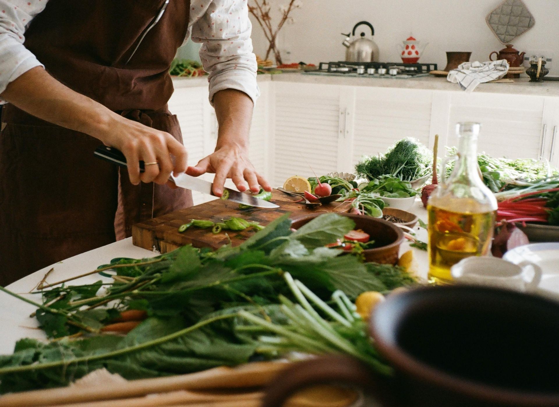 Person in apron chopping vegetables on a wooden cutting board in a kitchen with ingredients.