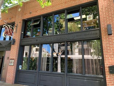 Brick storefront with black-framed windows and a dark awning, reflecting trees and nearby buildings