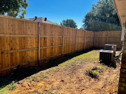 Wooden privacy fence along a narrow backyard with dry grass and an air conditioner unit on the right.