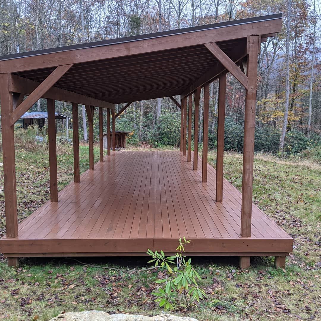 a wooden deck with a roof in the middle of a field