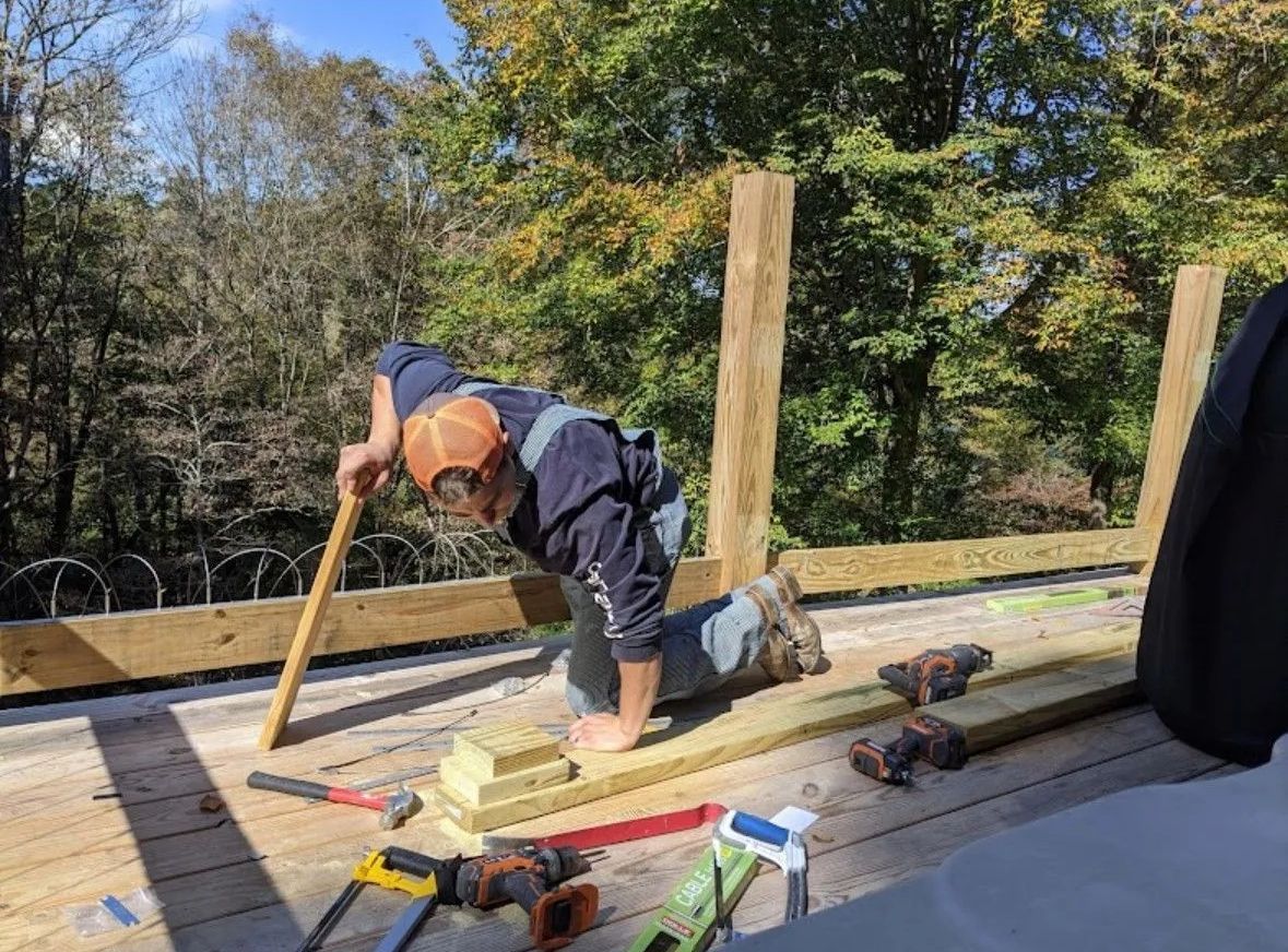 a man is kneeling down on a wooden deck working on a fence
