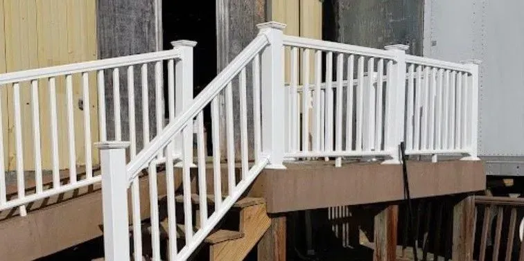 a white railing on a wooden deck with newly painted stairs leading up to it