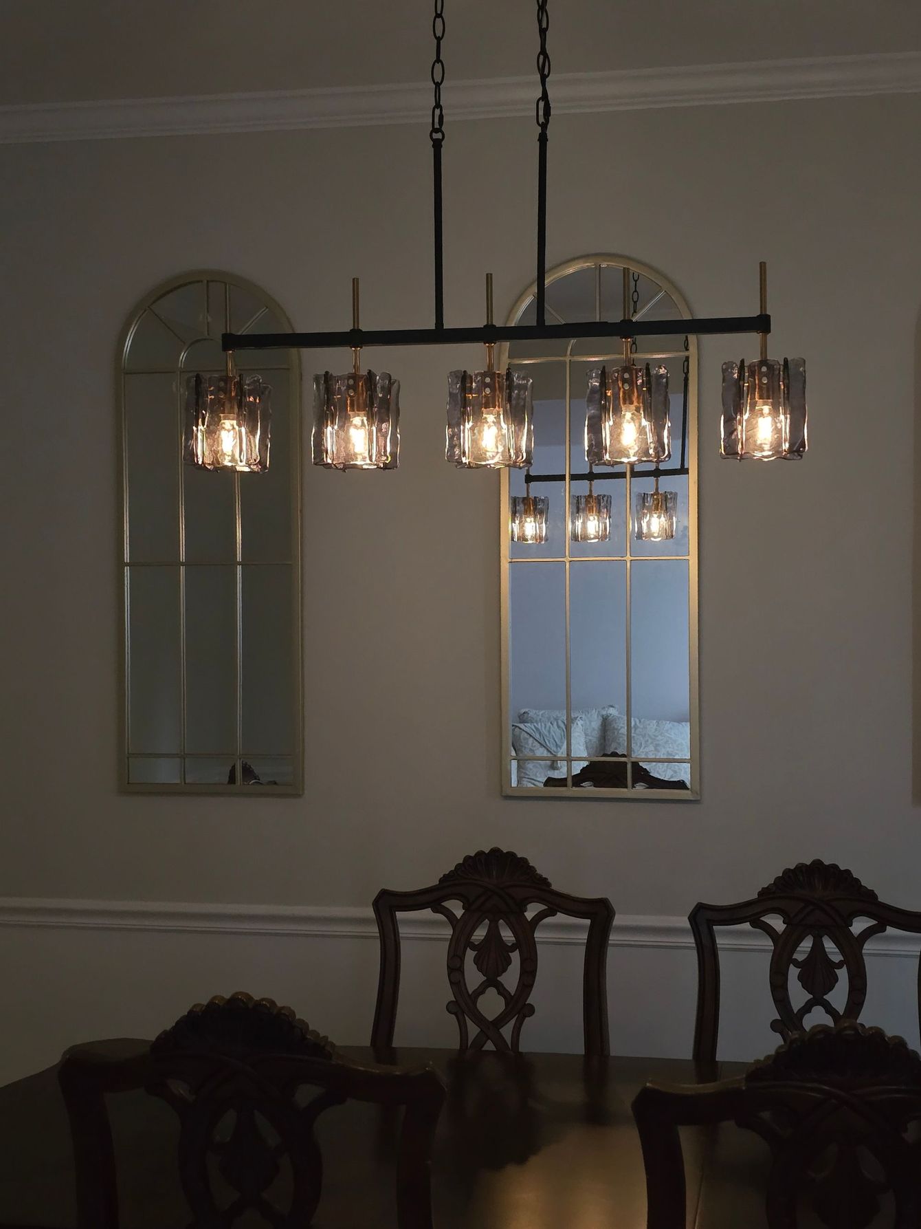 Elegant dining room with hanging glass pendant lights, mirrored wall decor, and dark wooden chairs
