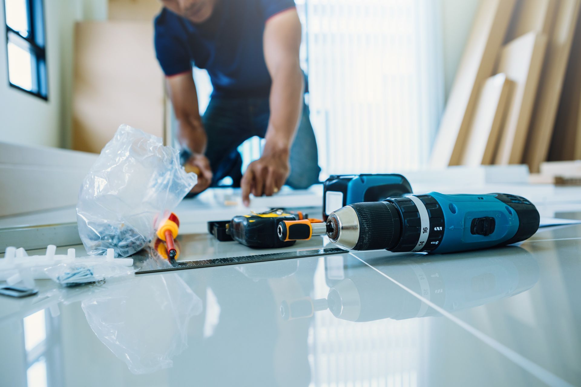 Person using a blue power drill on a glossy tiled floor in a workshop