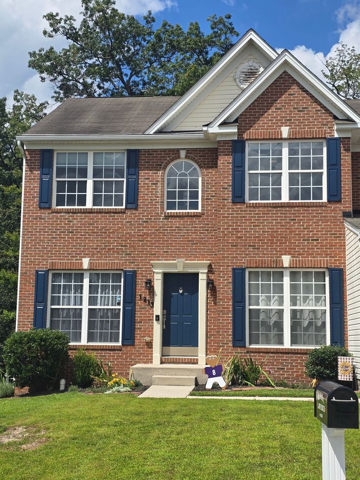 Two-story red brick house with blue shutters, white trim, and a black mailbox in front